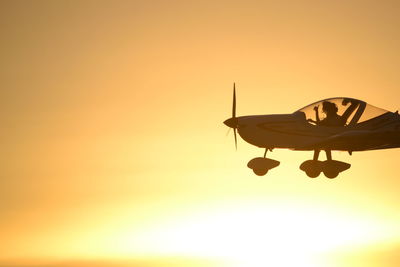 Silhouette airplane flying against orange sky