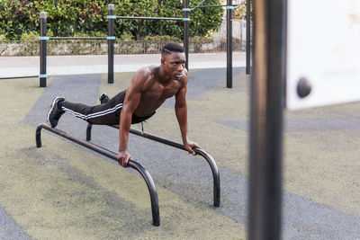 Determined black sportsman doing parallel bar dips on parallel bars during workout on sports ground