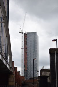 Low angle view of crane and buildings against sky