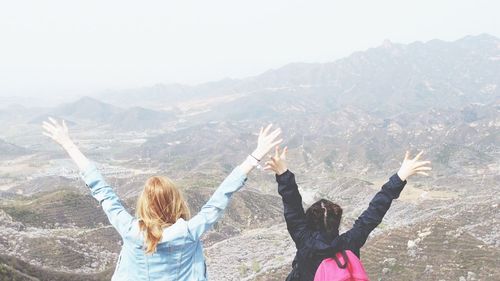 Rear view of women standing with arms raised against mountain range