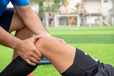 Low section of male physical therapist rubbing soccer player knee on field