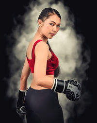 Young woman looking away while standing against black background