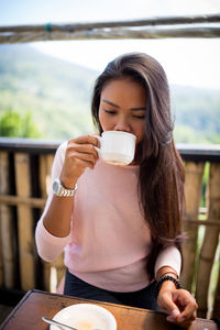 Full length of young woman holding drink sitting outdoors