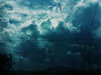 Low angle view of electricity pylon against cloudy sky