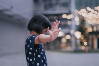 Side view of girl gesturing stop while standing outdoors