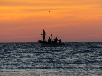 Silhouette people in sea against sky during sunset