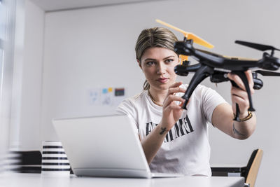 Young woman with laptop at desk holding drone