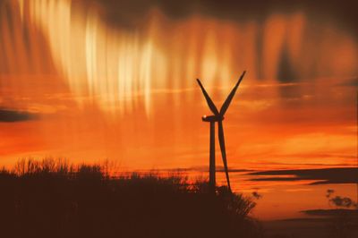 Wind turbine on field by sea against sky during sunset