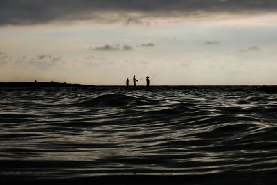 Silhouette people on sea against sky during sunset