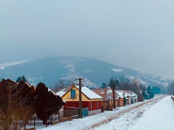 Snow covered houses by trees against sky