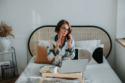 Young woman working remotely from home. sitting on the bed in the bedroom 