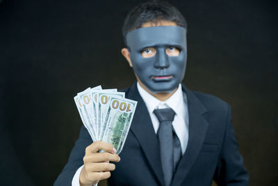 Close-up of businessman holding currency notes while wearing mask against black background
