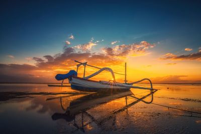 Boat moored on shore against sky during sunset