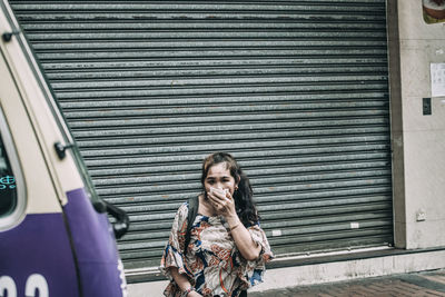 Portrait of woman standing against closed shutter
