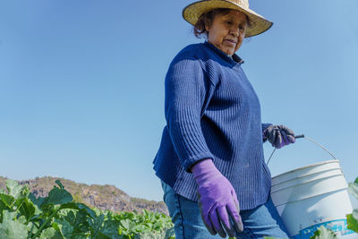 Woman holding bucket standing in field against sky