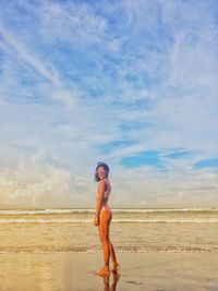 Young woman standing at beach against sky