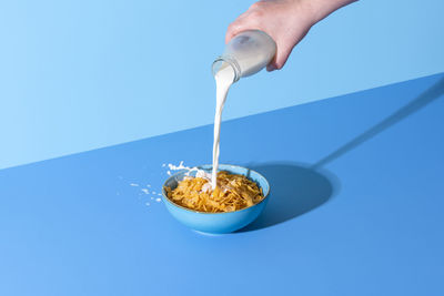 Pouring milk into a bowl with cornflakes cereals. cereals and milk isolated on a blue background