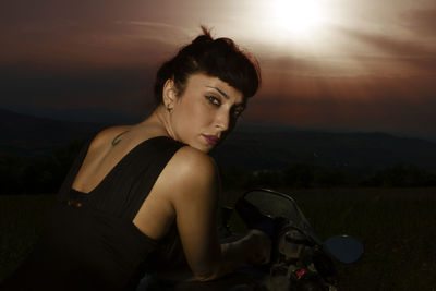 Portrait of woman with motorcycle on land against sky during sunset