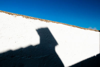 Shadow of person on wall against clear blue sky