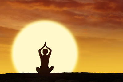 Woman doing yoga against orange sky