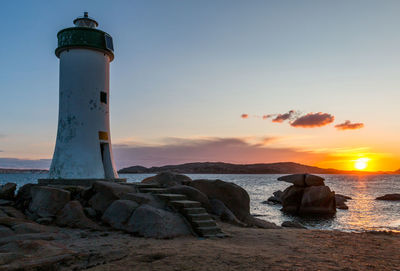 Lighthouse by sea against sky during sunset