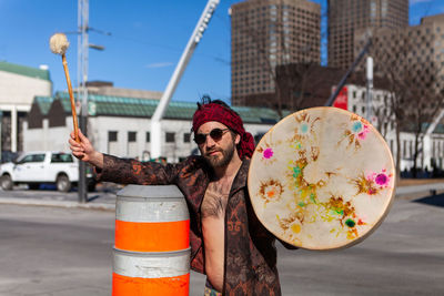 Portrait of man holding drum while standing at city