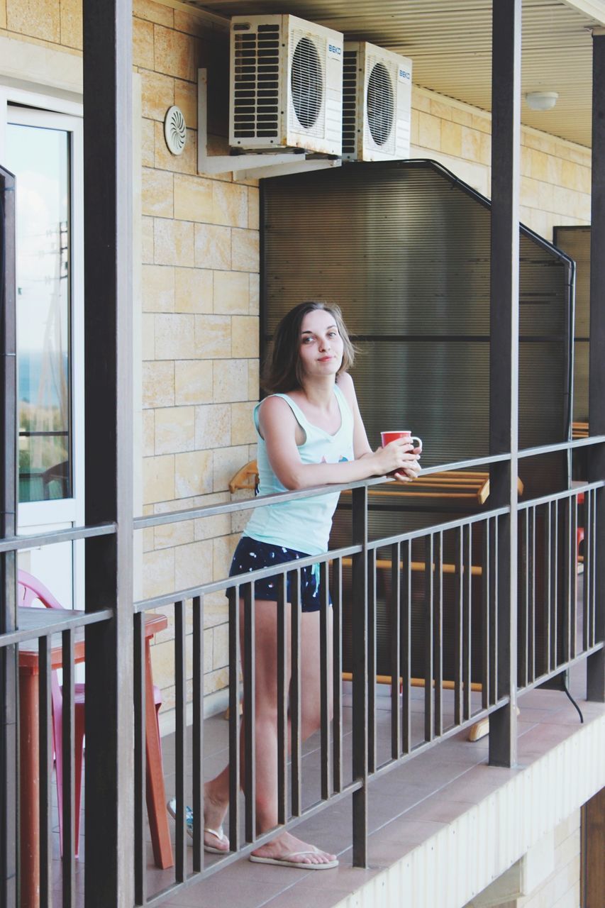 PORTRAIT OF SMILING WOMAN SITTING ON RAILING