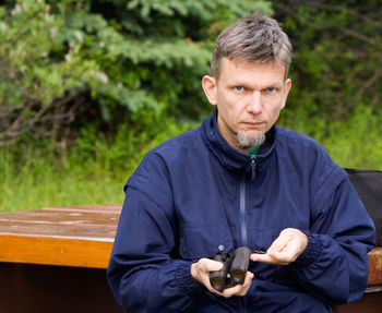 Portrait of man holding binoculars while sitting against trees