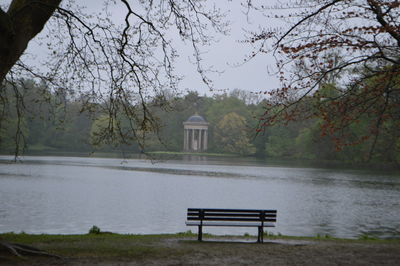 Empty bench by lake against trees