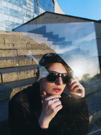 Portrait of young woman wearing sunglasses sitting outdoors