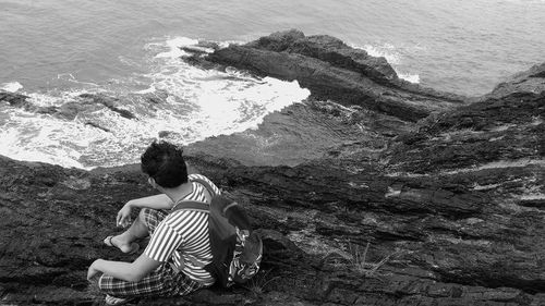 Rear view of couple sitting on rock by sea