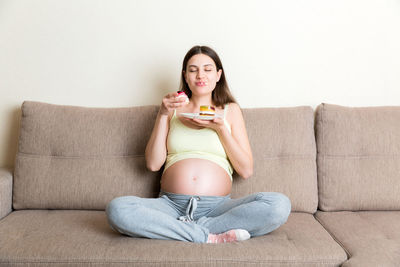 Pregnant woman eating food while sitting on sofa
