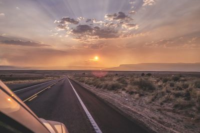 Road amidst field against sky during sunset