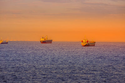 Boat sailing on sea against orange sky