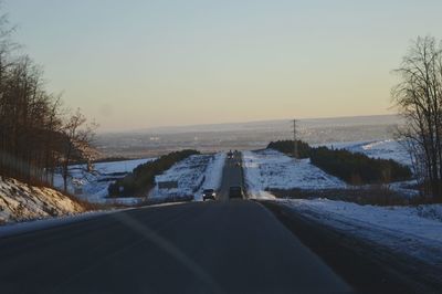 Road amidst trees against clear sky during winter