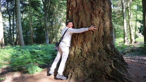 Man standing by tree trunk in forest