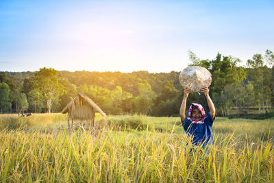 Portrait of farmer holding asian style conical hat on field against sky