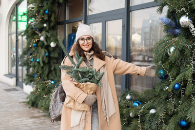 A smiling woman in a coat holds a christmas tree toy of a christmas store