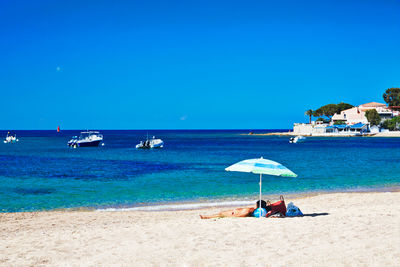 Man sitting on beach against clear blue sky