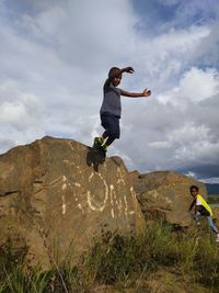 Rear view of kid jumping on rock against sky