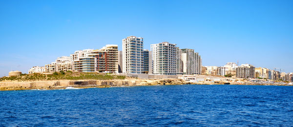 Buildings by the seaside against clear blue sky