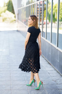 Full length of young woman standing on footpath in city