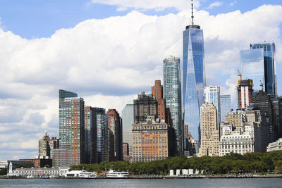 Low angle view of modern buildings by river against cloudy sky