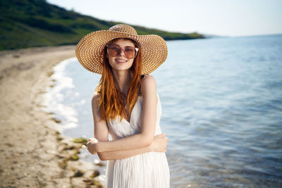 Young woman wearing hat standing against sea