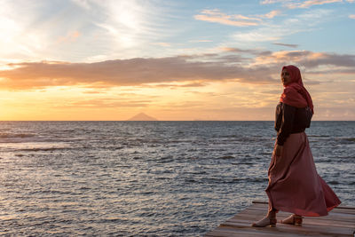 Woman standing on beach against sky during sunset