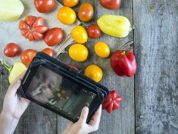 Cropped image of woman photographing vegetables through digital tablet