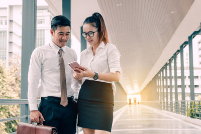 Colleagues using mobile phone while standing in corridor