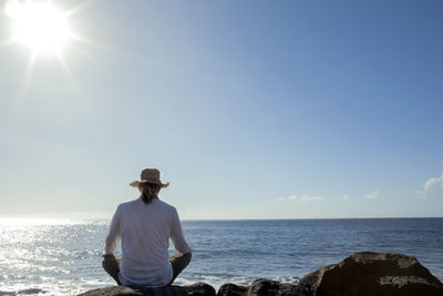Mature man sitting on rock in front of sea during sunny day