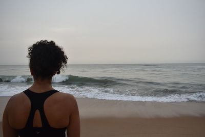 Rear view of woman looking at beach against sky during sunset