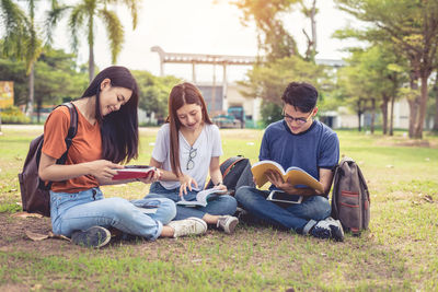 Friends studying while sitting on grassy field at park